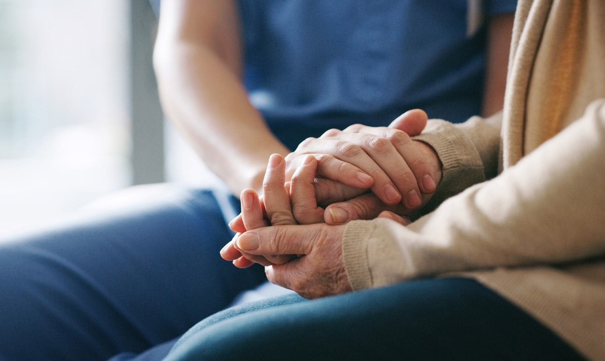 A nurse in scrubs holding an older person's hands in both of hers