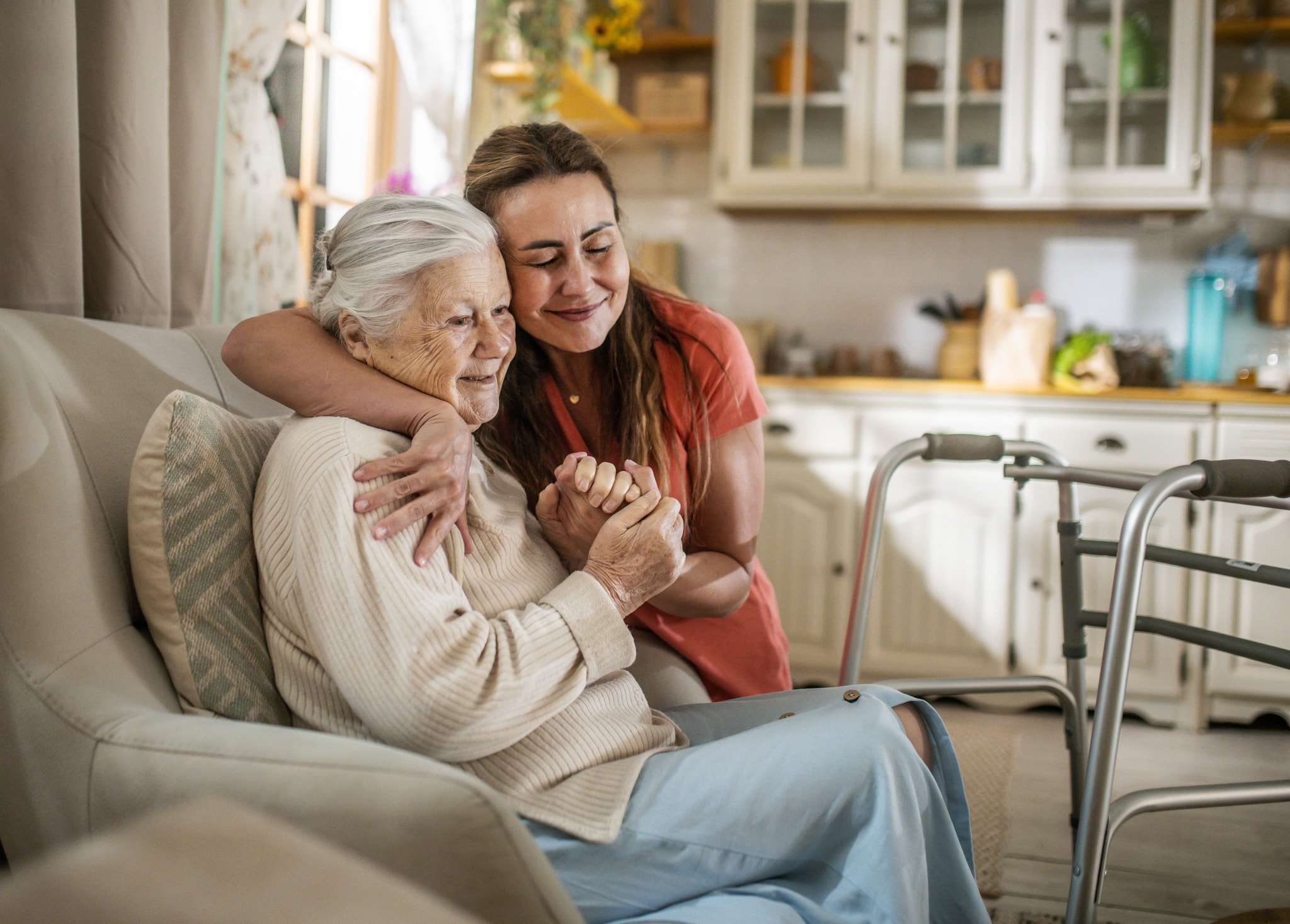 A support worker with her arm around an older woman in her armchair, a walking frame beside them