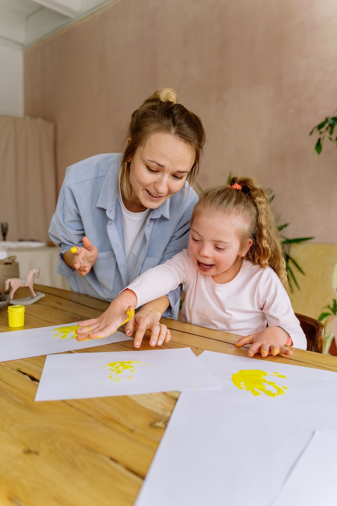 A support worker and a young girl with Down syndrome making handprints in yellow paint